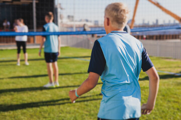 Obraz premium Volleyball game, junior teenage school team of kids play volleyball, players on the outdoor playground with net and green lawn grass court, sports children team during the game, summer sunny