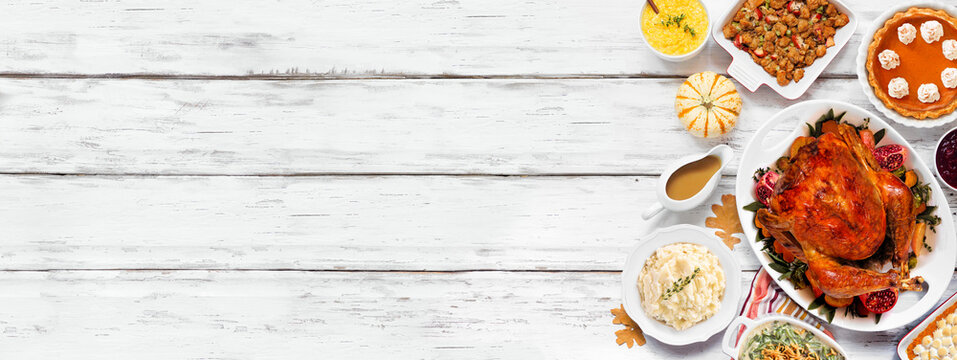 Traditional Thanksgiving turkey dinner. Top view side border on a rustic white wood banner background. Turkey, mashed potatoes, stuffing, pumpkin pie and sides.