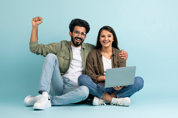 Happy multiethnic couple gambling online, using laptop on blue