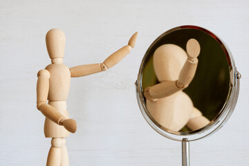 A light wooden mannequin looks in the mirror, looking for its image. The concept is self-knowledge,...
