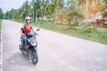 Tropical travel and transport. Happy young woman in helmet riding scooter on the road with palm...