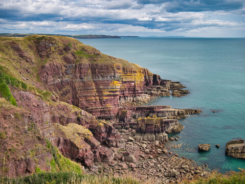 Coastal red cliffs near Manorbier in Pembrokeshire, Wales, UK - the vertically inclined rock strata of the bedrock is of the Milford Haven Group - Argillaceous rocks and sandstone, interbedded.