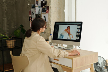 Young female photographer sitting in front of computer screen and reviewing new shots of gorgeous African American fashion model