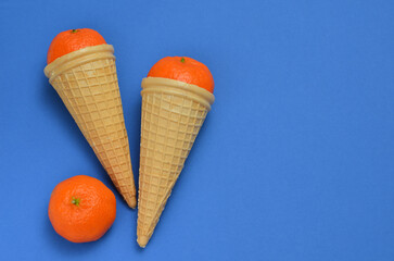 bright food background with tangerines in waffle cones on a blue background, copy space