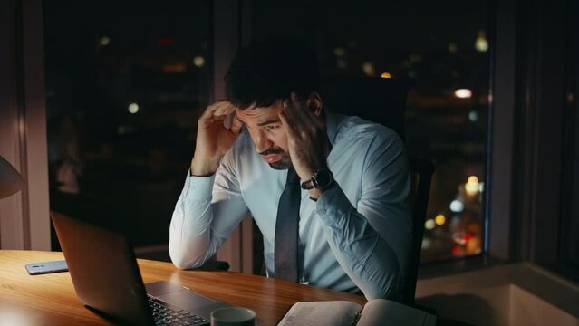 Frustrated professional employee working late evening in dark office. Man tired