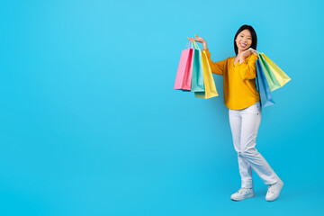 Happy young korean woman showing her purchases, blue background