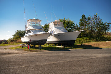 Motor boats stand on land under the open blue sky in the parking lot at the pier.