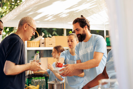 Friendly voluntary individuals helping the less fortunate, providing charitable support through food distribution. Young people volunteering and fighting poverty at an outdoor hunger relief program.
