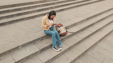 Fototapeta premium Traveler girl using looking mobile phone sitting on the steps of an old building in the historical part of an old European city, view from above