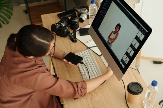 Above angle of young freelance photographer sitting in front of computer screen with new shots of fashion model taken during photo session