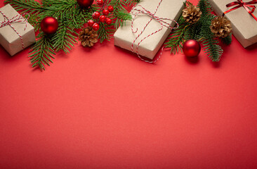 Fototapeta na wymiar Christmas or New Year celebration red paper festive background with decoration fir tree, wrapped present boxes, cones, berries, sparkly red balls. Space for text..