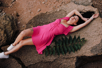 Beautiful woman in pink dress lying on a big stone at seashore
