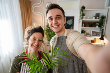 Fototapeta premium Couple caucasian man and woman wife and husband planting flowers together taking care of home plants real people domestic life family gardening concept take selfie photo with smartphone UGC