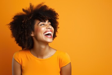 portrait of a smiling young woman laughing. young black woman with curly hair laughing on orange background