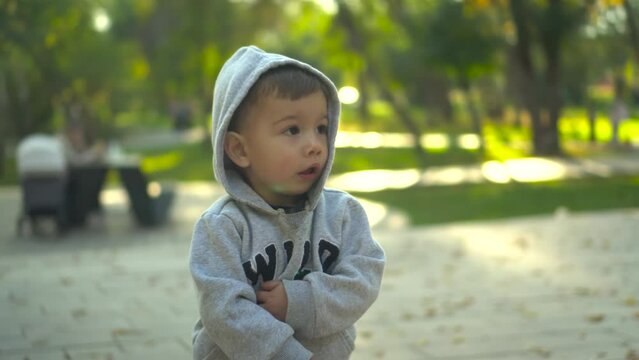 A two-year-old boy stands in the park and looks