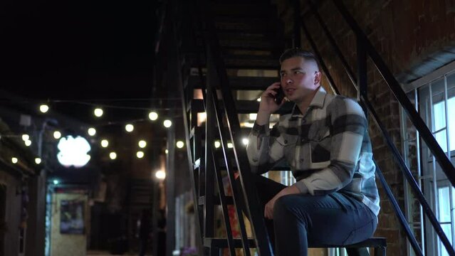 A young man sits on a fire escape and texts