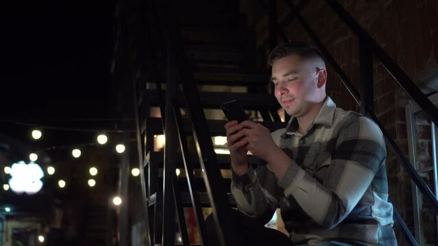 A young man sits on a fire escape and texts