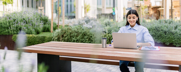 Young business woman studying master on laptop sitting outside of his office. Millennial adult student listening training online business class on computer. Banner aspect. - obrazy, fototapety, plakaty