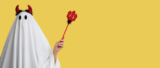Person in costume of ghost with devil horns on yellow background with space for text. Halloween...