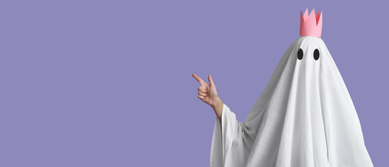Person in costume of ghost pointing at something on lilac background with space for text. Halloween celebration