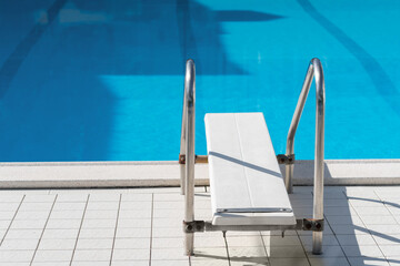 Grab bars ladder in the blue swimming pool, empty chaise longue