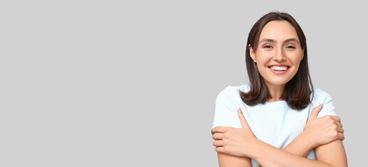 Young woman hugging herself on light background with space for text