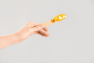 Female hand holding spatula with sugaring paste on light background
