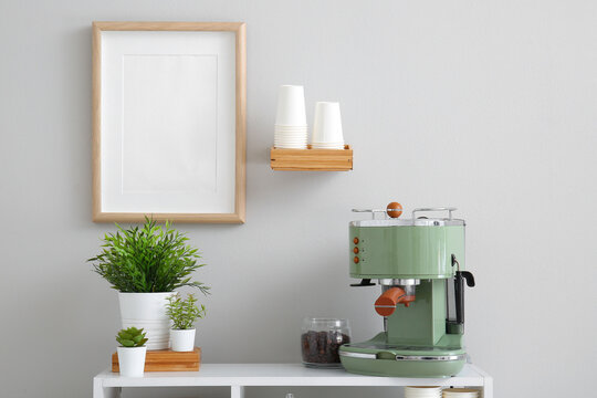 Modern coffee machine, jar with beans and houseplants on table near white wall