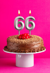 Number 66 candle - Chocolate cake on pink background