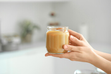 Young woman with jar of nut butter in kitchen, closeup