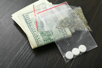 Plastic bags with drugs and money on dark wooden background