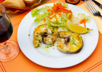 Sliced roasted hake served with fresh vegetable salad and lemon