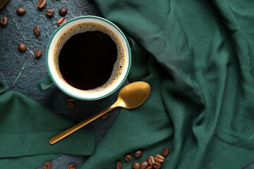 Cup of coffee with spoon, scattered beans and cloth on dark turquoise background