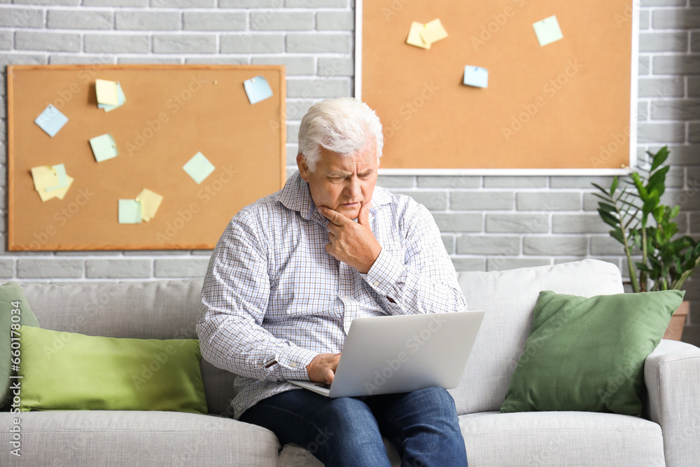 Canvas Prints Thoughtful senior man using laptop on sofa at home