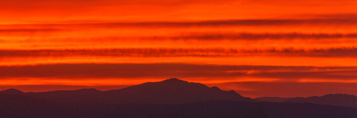 Panorama of orange warm colorful sky from sunset over silhouette of mountain landscape