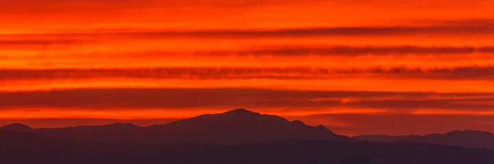 Fototapeten Panorama of orange warm colorful sky from sunset over silhouette of mountain landscape © Sebastian