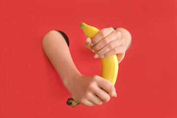 Female hands with fresh banana on red background. Sex education concept