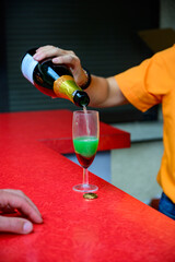 Making of cocktail based on champagne sparkling wine with strawberry syrup, orange juice and blue curacao liquor