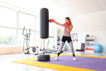 Young woman training with punching bag in gym. Concept of self defense - obrazy, fototapety, plakaty