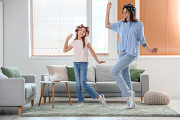 Little girl and her mother with hair curlers dancing at home