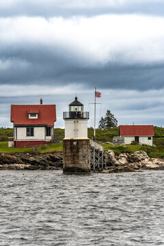 White lighthouse and red-roofed keeper's buildings on a small rocky island off the coast of Maine