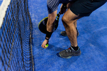 Man playing a padel game in a blue court with his racket and ball