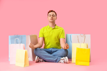 Young man with shopping bags meditating on pink background