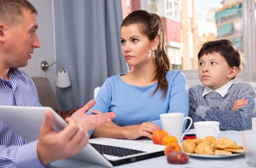 Obraz premium Man explaining details of documents to his worried wife and preteen son while sitting with laptop at home table