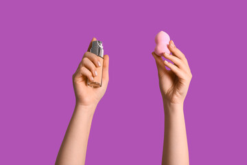Female hands with makeup sponge and bottle of foundation on purple background