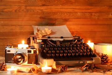 Vintage typewriter, photo camera, keys, pine cones, burning candles and autumn leaves on wooden background