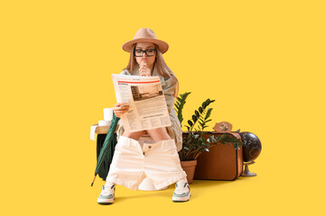 Female traveler reading newspaper on toilet bowl against yellow background