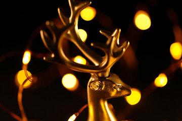 Christmas background. Golden deer and g bokeh of garlands on a black background.Glowing decorative...