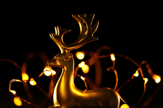 Christmas background. Golden deer and golden bokeh of garlands on a black background.Glowing decorative object. Christmas deer and garland on a dark background. 