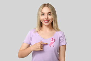 Young woman with pink ribbon on grey background.  Breast cancer awareness concept